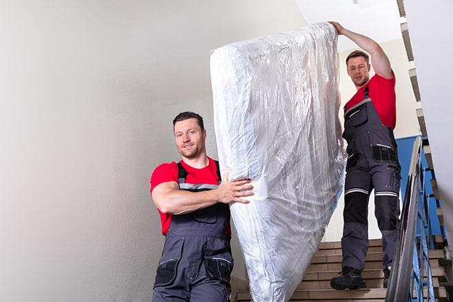 two people carrying a box spring out of a room in Benbrook